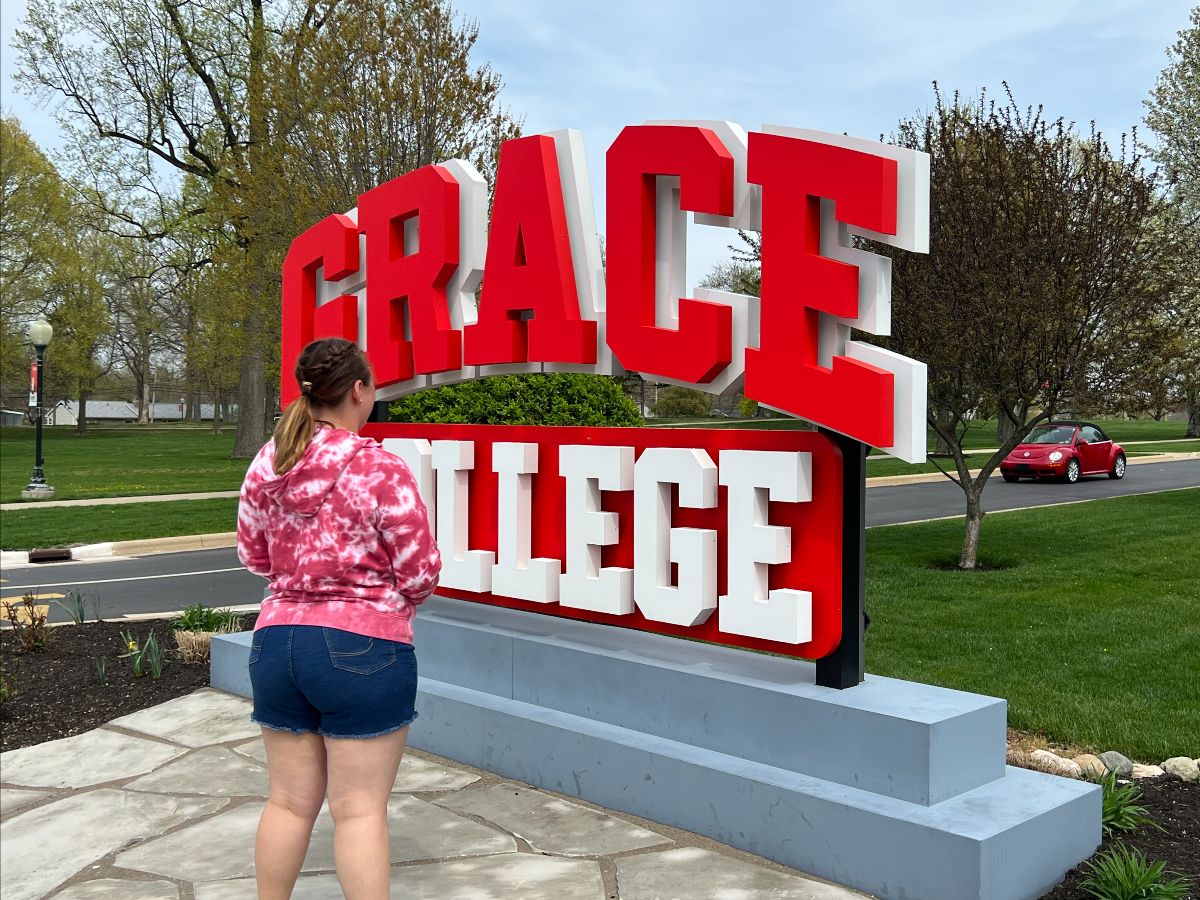 A figure standing thoughtfully in front of the Grace College sign.